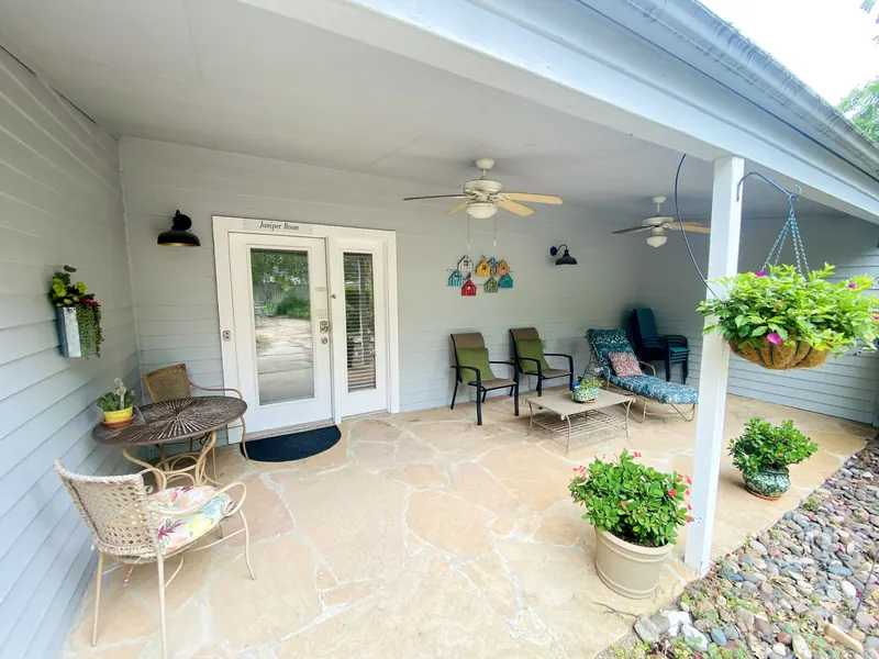 The covered patio outside the Juniper room at Comal Inn, with chairs, a table and hanging plants