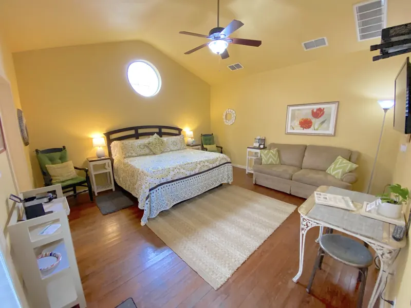 A guest room at Comal Inn with a king bed, sofa, writing desk and hardwood floors
